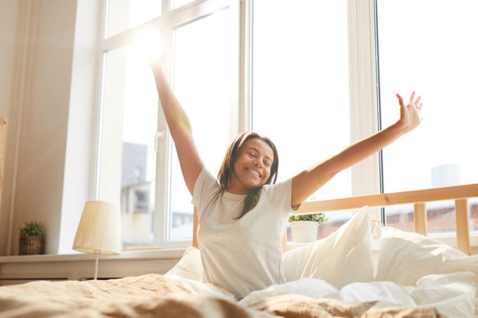 Mixed-Race woman stretching sitting in bed lit by sunlight girl black morning sleep healthy