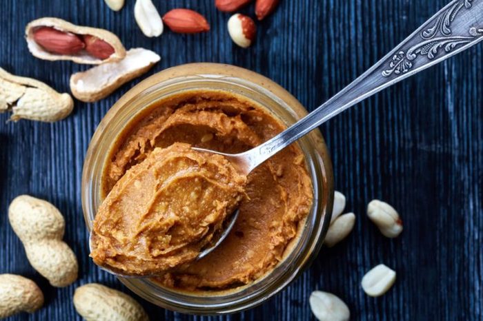 spoonful of crunchy peanut butter over a jar of it, surrounded by peanuts