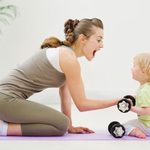 woman on yoga mat holding weights and playing with baby
