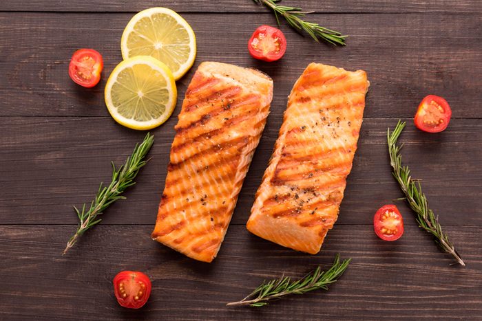 Two grilled salmon filets with rosemary, tomatoes, and lemon slices