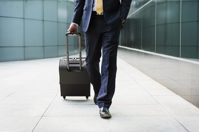 man in business suit walking with roller suitcase