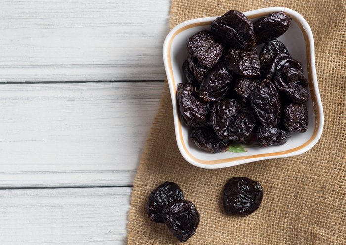 Prunes in bowl on wooden white background