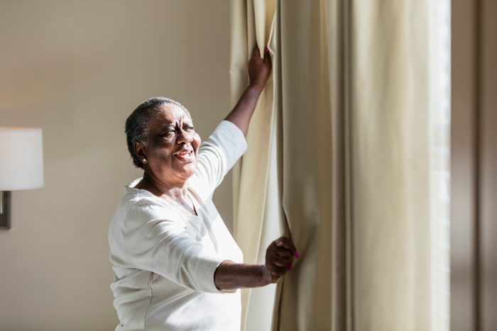 senior woman opening window curtains at home