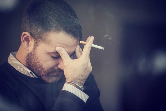 unhappy white man with beard smoking with head in hand