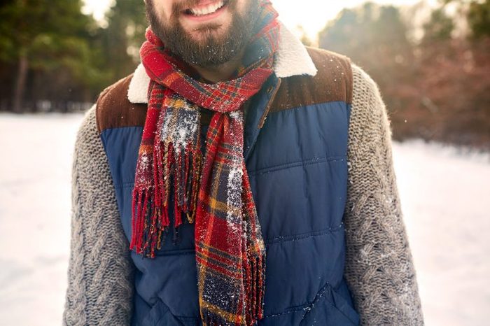 Bearded man in a scarf and winter vest in the snow.