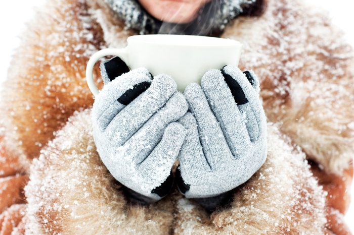 Woman in a fur trimmed collar and gloves holding a mug.
