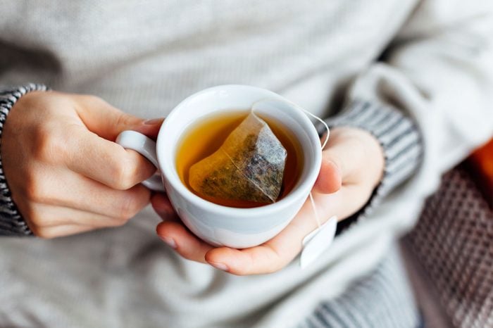 Person in a gray sweater holding a mug of tea.