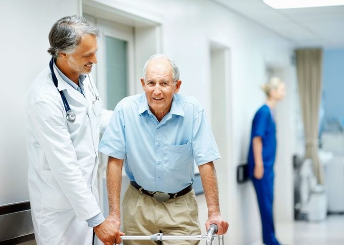 doctor helping an elderly man using a walker in a hospital hall