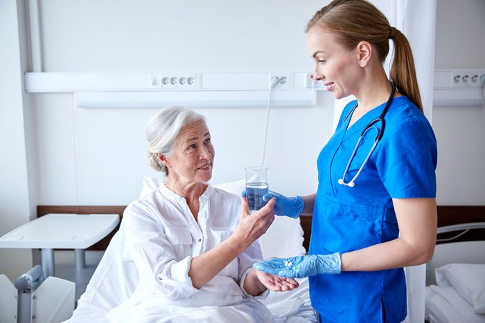 young female nurse handing an elderly patient pills and water