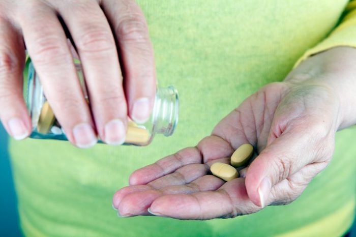 person shaking tablets out of a bottle into hand