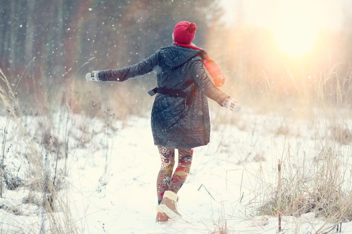 woman in coat and hat walking in a snowy field
