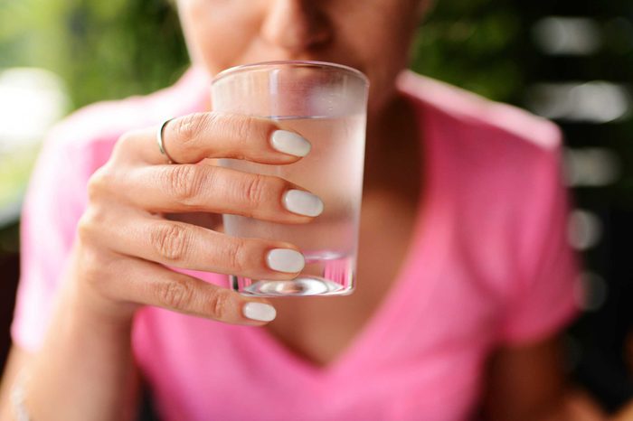 Woman in a pink shirt drinking a glass of water.