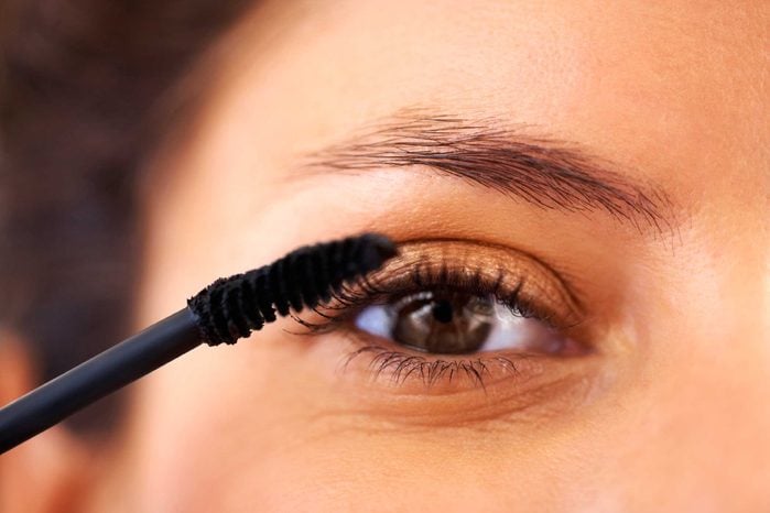 Woman applying mascara to her eyelashes.