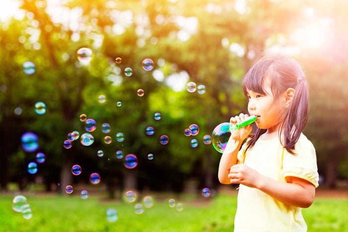 Young girl blowing soap bubbles outside.