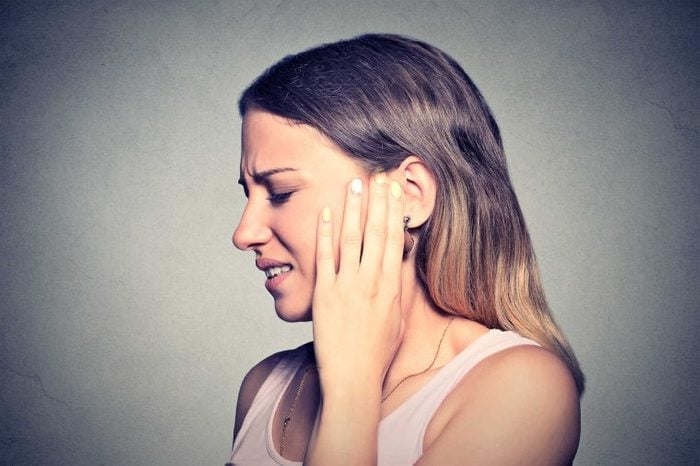 A woman turned to the side, holding up her left hand to her left ear as if it's causing her pain.