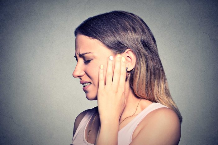 A woman turned to the side, holding up her left hand to her left ear as if it's causing her pain.