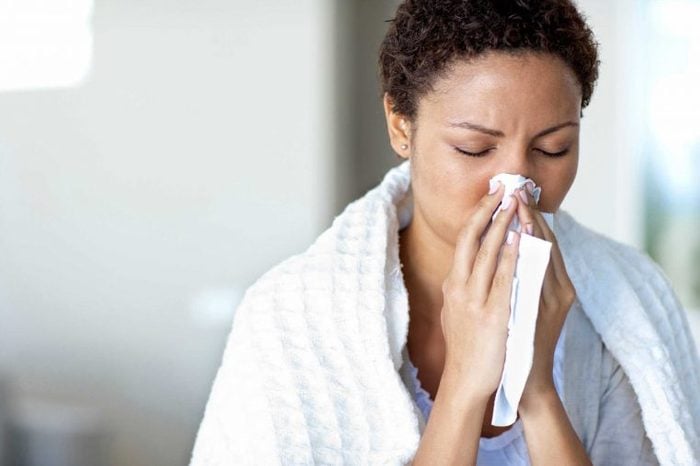 A woman wearing a white towel blowing her nose into a tissue.