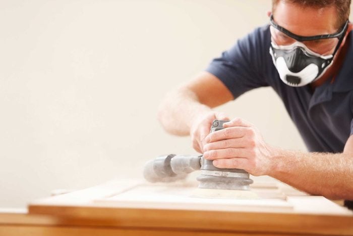 Man wearing goggles and face mask while sanding wood.