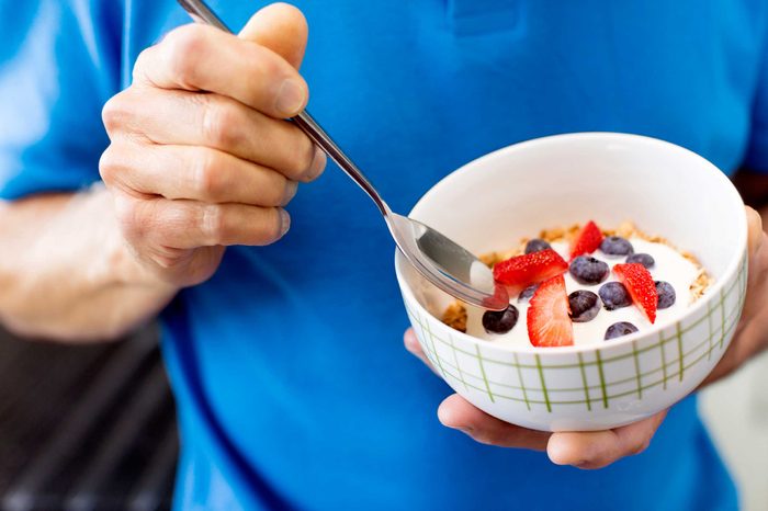 Man eating a bowl of yogurt and fruit with a spoon.