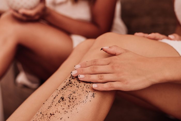 close up of woman applying coffee scrub on leg