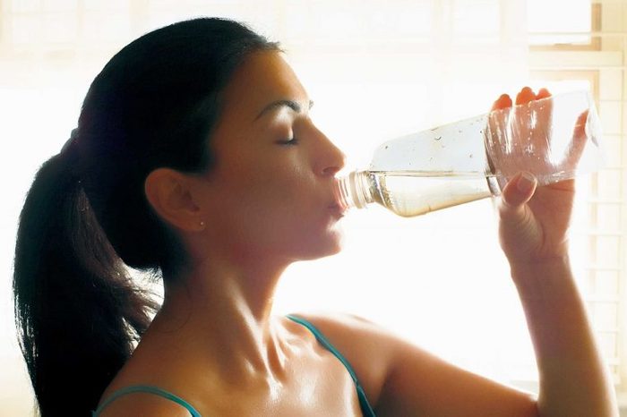 Woman in a tank top drinking water from a water bottle.