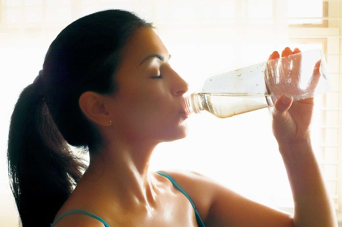 Woman in a tank top drinking water from a water bottle.
