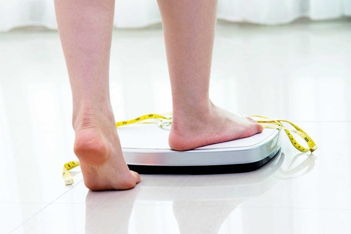 woman stepping scale with measuring tape