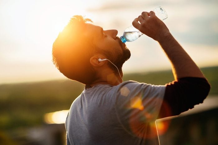 man with earbuds outside, drinking from a bottle of water