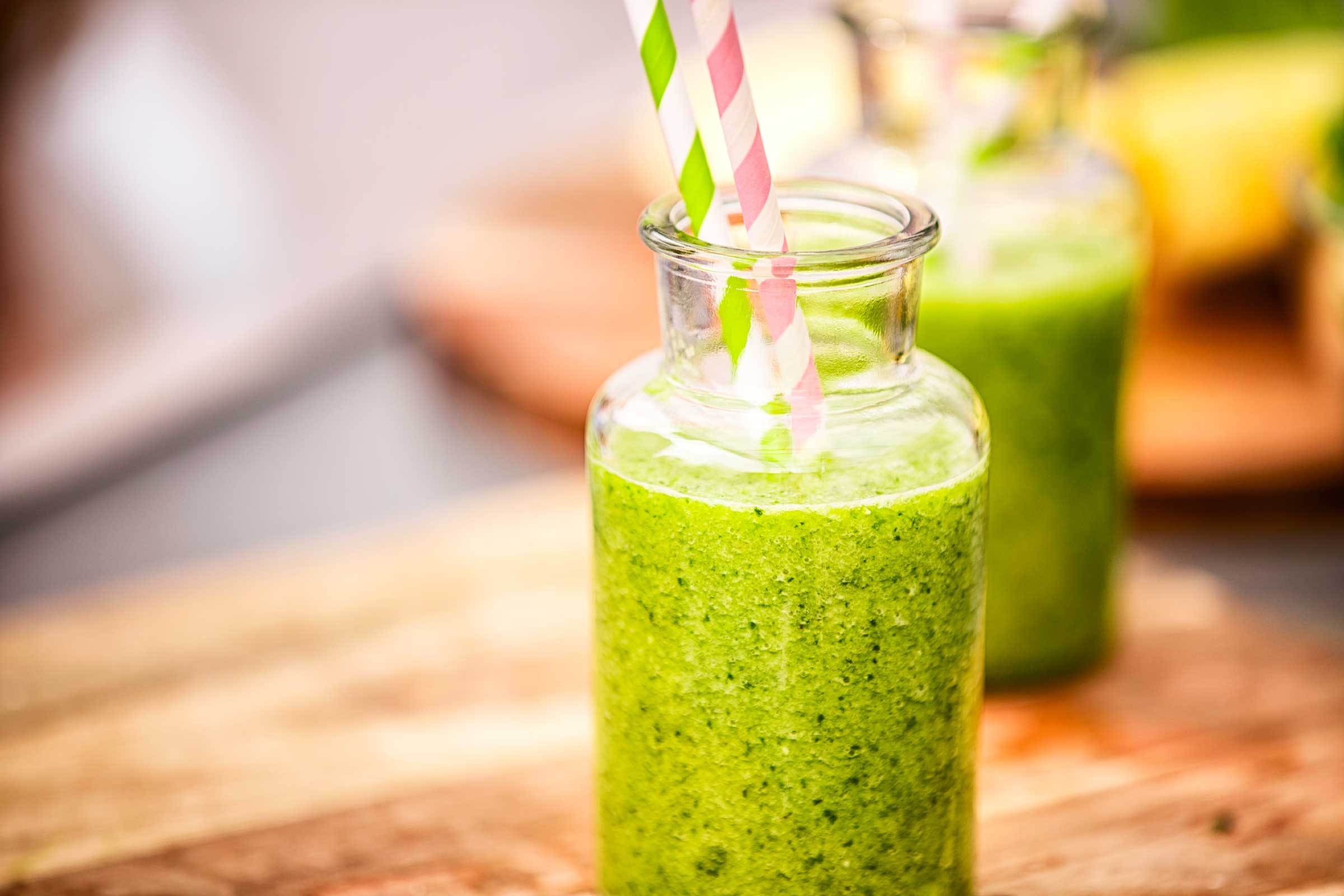 green smoothie in a jar-like glass with two striped straws