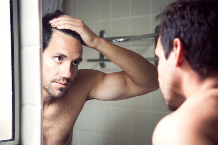 man looking at his hairline in a mirror