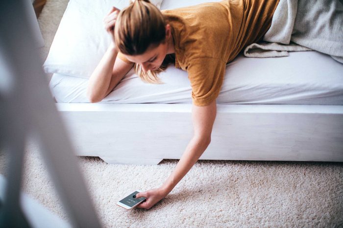 Woman lying on a bed propping her head up with one hand and using her cellphone in the other hand.