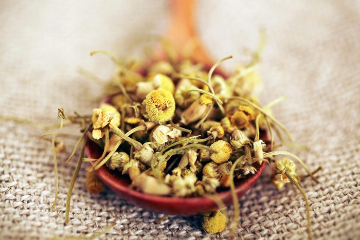 dried chamomile in a wooden spoon on burlap