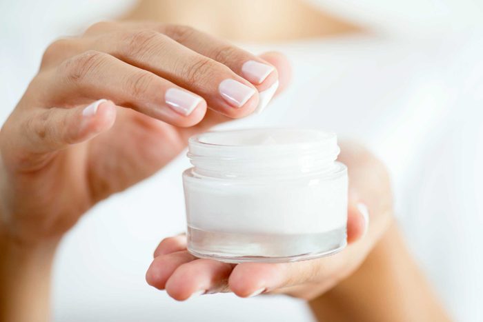 Woman dipping her fingertips into a jar of moisturizer.