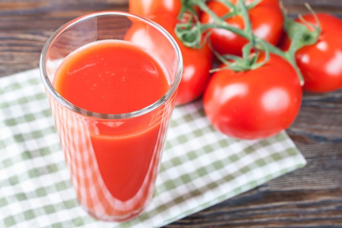 Glass of tomato juice with ripe tomatoes behind it.