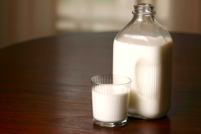 Glass of milk next to a glass bottle of milk.