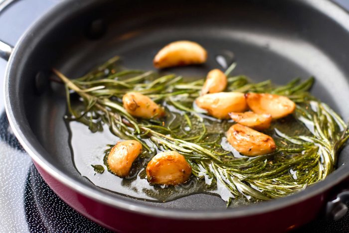 rosemary stems and garlic bulbs in oil on the stove