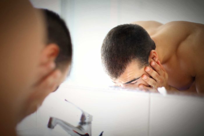 Man washing his face in the bathroom sink.