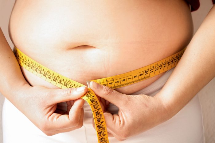 person measuring belly fat with tape measure