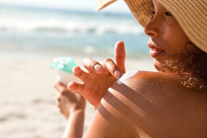 Dark-skinned woman applying sunscreen.