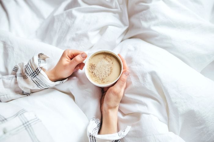 a person in bed holds warm drink 