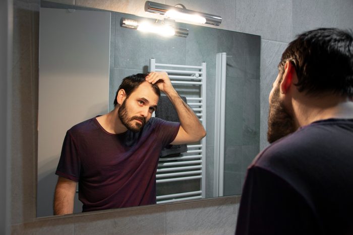 man looking at hair line in bathroom mirror