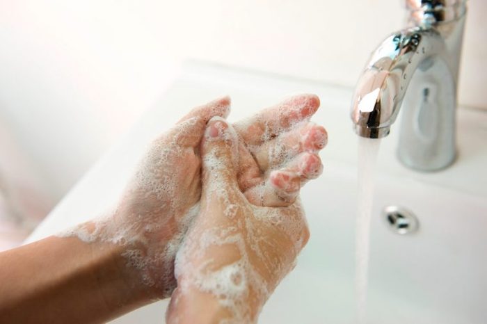 Pair of hands that are lathered in soap near a faucet of running water.