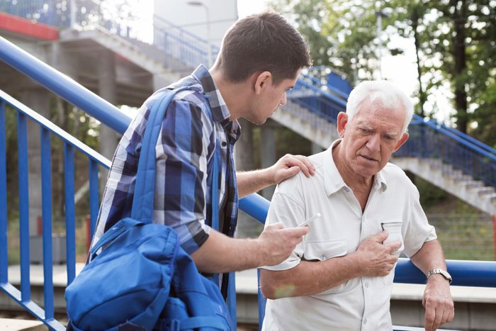 young man helping older man clutching chest