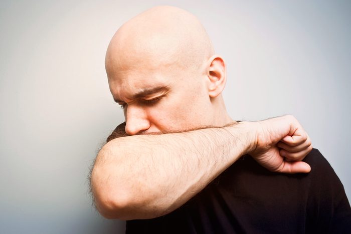 man with shaved head coughing into the crook of his arm
