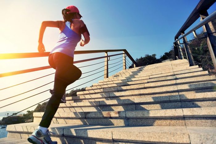 Woman in activewear jogging up a flight of outdoor stairs as the sun is rising.