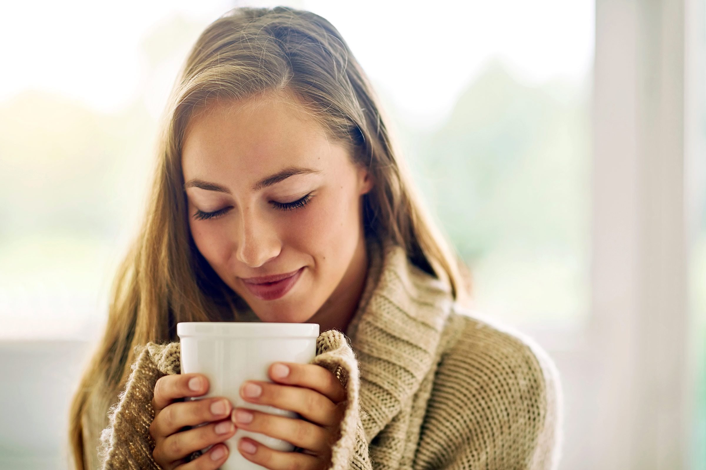 woman holding a cup of coffee with both hands close to her face