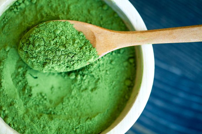 Bowl of green spirulina powder and a wooden spoon.