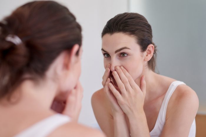 woman closely looking at face in mirror