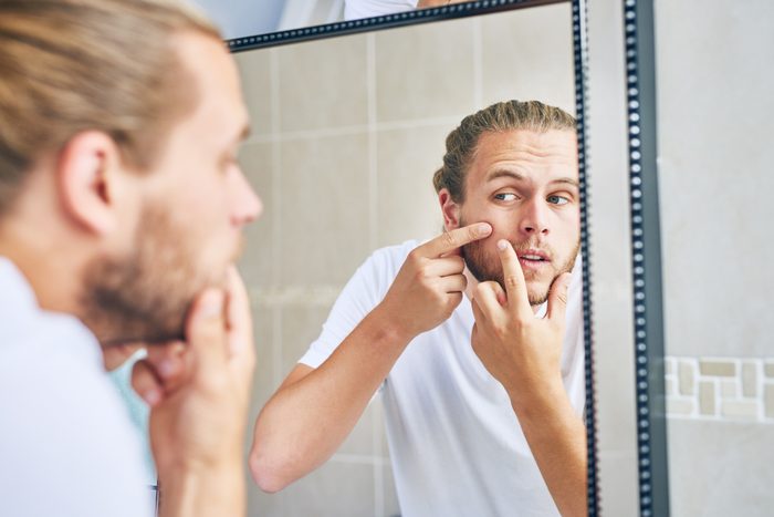 man squeezing pimple in mirror