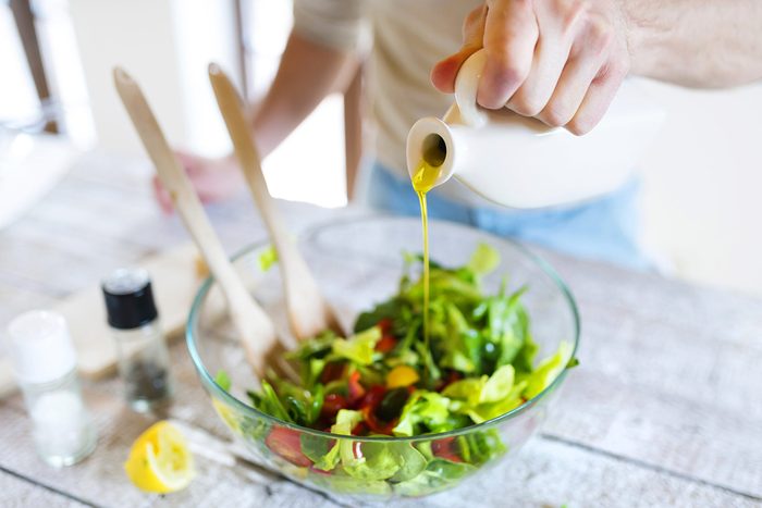 person drizzling olive oil on salad